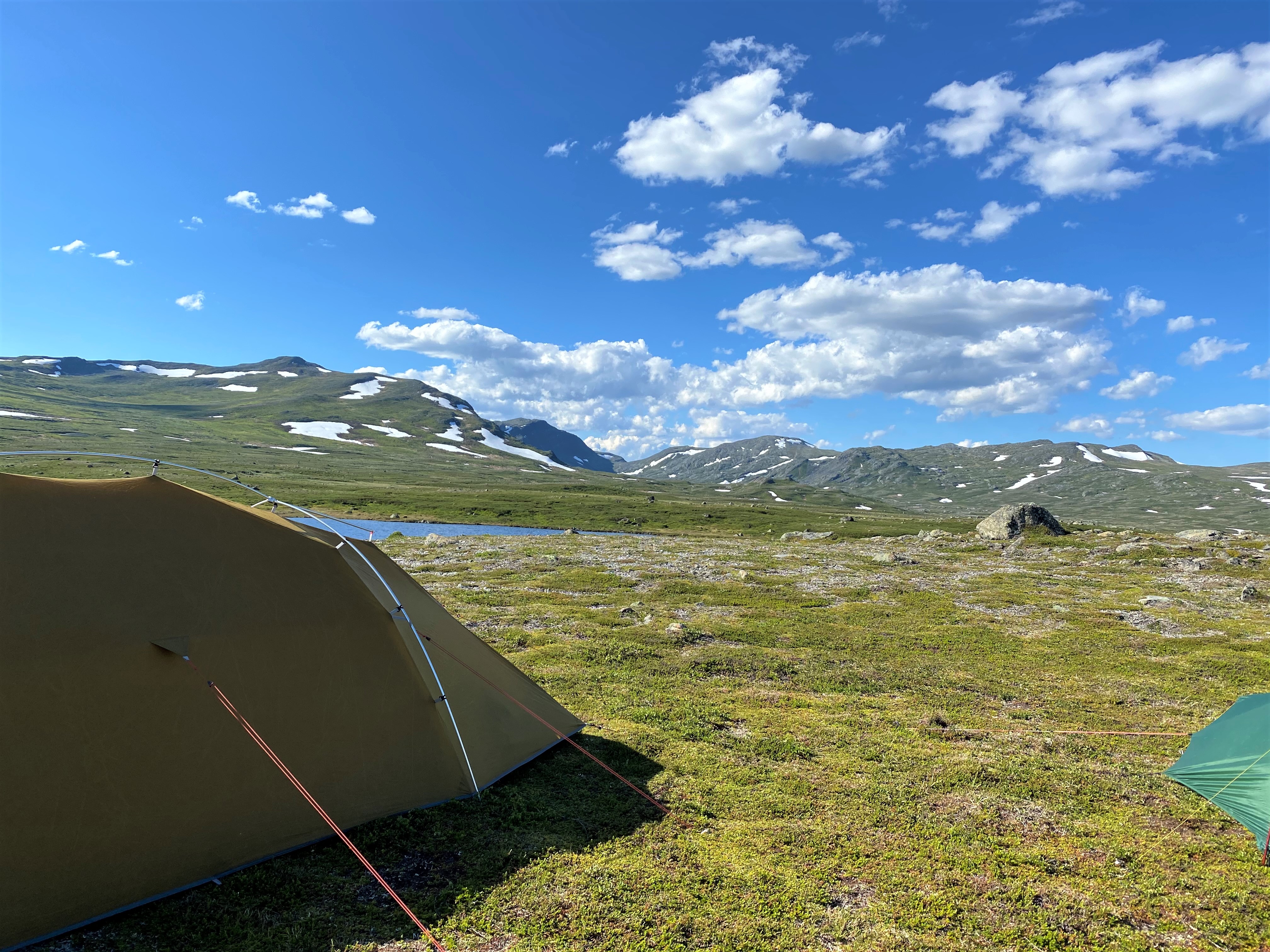 Utsiktsbild med tält och fjällsjö i förgrunden